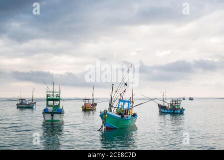 Bunte schäbige Boote, die auf dem ruhigen Wasser des Meeres schwimmen Hintergrund des stürmischen Himmels Stockfoto