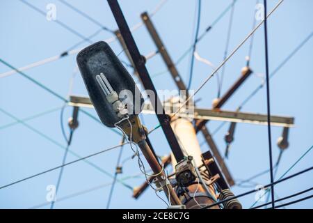 Von unten der Straßenlaterne, die auf dem Strommast mit hängt Viele Kabel gegen blauen Himmel Stockfoto