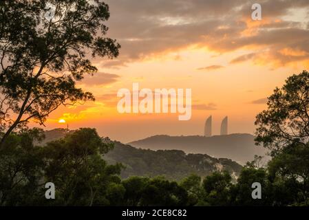 Spektakuläre Landschaft von grünen Hügeln und Silhouetten von modernen Wolkenkratzern Von Xiamen Stadt in China während des bewölkten Abendhimmels Sonnenuntergangszeit Stockfoto