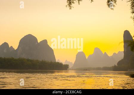 Erstaunliche Ansicht der Silhouetten der Berge und des plätschernden Wassers während des hellen Sonnenunterges im Yangshuo Bezirk, China Stockfoto