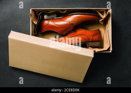 Herrenschuhe in offener Box, isoliert auf schwarzem Hintergrund. Öffnen Sie den Schuhkarton. Neue Schuhe aus dem Laden. Braune Schuhe aus echtem Leder. Die Aussicht von Stockfoto