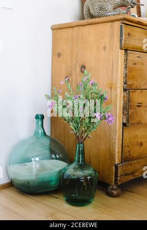 Set aus verschiedenen Glasvasen mit Blumen und Sand arrangiert In der Nähe verwitterten Holzschrank in gemütlichen Raum mit Retro-Interieur Design Stockfoto