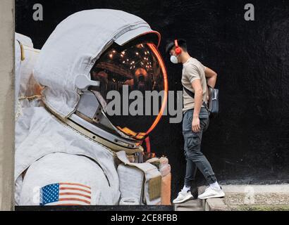 Hongkong. August 2020. HONGKONG, HONGKONG SAR: 31. AUGUST 2020. Ein Mann mit einer Maske geht an dem Bild eines Astronauten vorbei, der seine Maske in Hongkong trägt. Obwohl das Tragen von Masken im Freien etwas entspannt war, trägt jeder auf der Straße immer noch eine. Die Street Art wirbt für den französischen Künstler, Vincent FournierÕs Ausstellung, Space Project in der Galerie La Galerie in Aberdeen Street Hong Kong. Alamy Live Nachrichten/Jayne Russell Kredit: Jayne Russell/Alamy Live Nachrichten Stockfoto