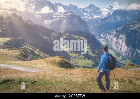 Rückansicht des gesichtslosen männlichen Reisenden in legerer Kleidung und Rucksack genießen herrliche Kamm mit Gras unter dem Himmel bedeckt in Nachmittag Stockfoto