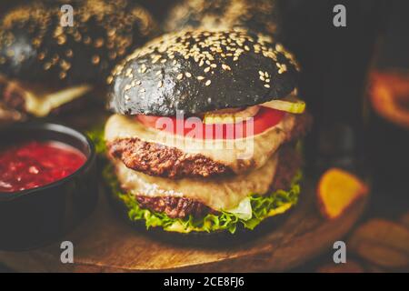 Schwarze doppelte Burger mit Käse. Cheeseburger aus Japan mit schwarzem Brötchen auf dunklem Hintergrund Stockfoto