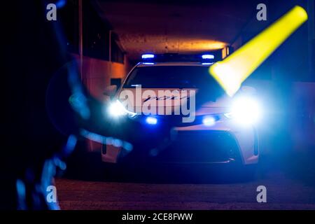 Rückansicht des Getreidepoliziers stehend mit beleuchtetem Verkehr Zauberstab vor dem Streifenwagen mit Blinklicht an Nacht Stockfoto