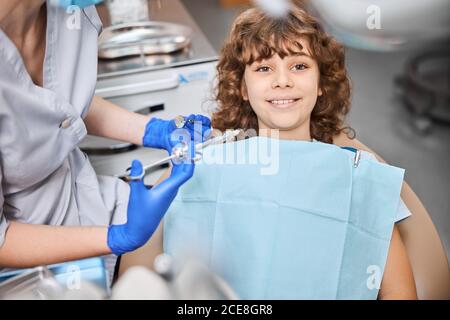 Netter Junge sitzt im Zahnstuhl und lächelt nach der Anästhesie Stockfoto