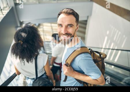 Glücklich lächelnder bärtiger Mann auf der beweglichen Treppe im internationalen Flughafen Stockfoto