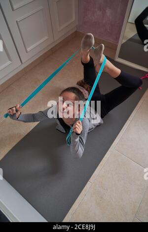 Von oben Mädchen tun Bogen Pose mit elastischen Band während Dehnung der Wirbelsäulenmuskulatur auf der Matte Stockfoto