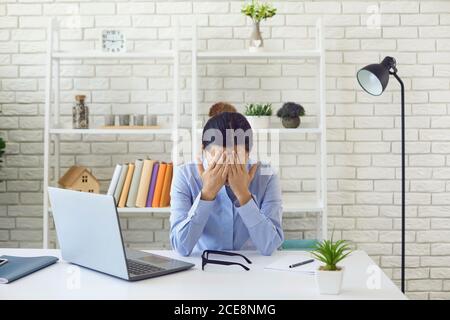 Erschöpfte junge Frau arbeitet Überstunden im Büro. Weibliche Angestellte, die an ihrem Schreibtisch unter Arbeitsstress leidet Stockfoto