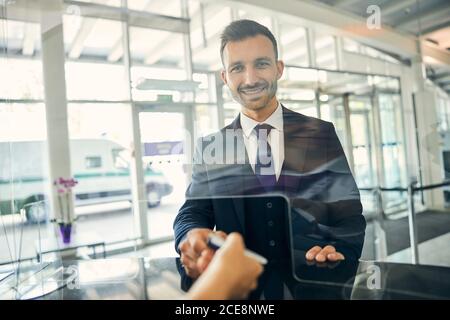 Fröhlicher Mann, der Reisedokumente hält, lächelt an der Kamera Stockfoto