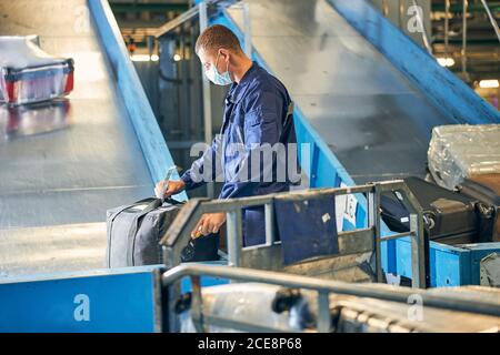 Mann im Overall, der ein Etikett auf dem Gepäck der Passagiere überprüft Stockfoto