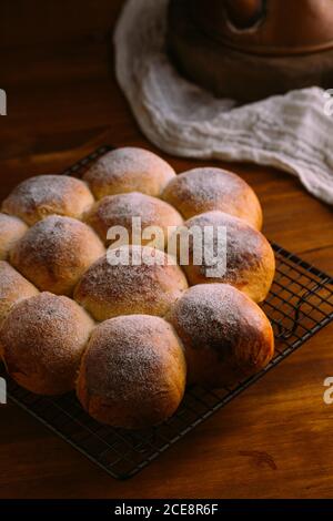 Von oben identische appetitliche Brötchen mit runder Form und goldene Oberfläche mit Zuckerpulver auf Metall Kühlgestell verziert Auf Holztisch Stockfoto