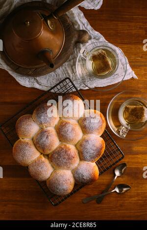 Von oben identische appetitliche Brötchen mit runder Form und goldene Oberfläche mit Zuckerpulver auf Metall Kühlgestell verziert Auf Holztisch Stockfoto