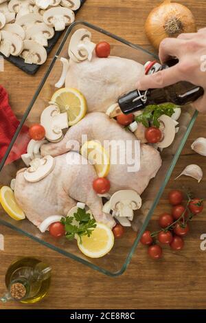 Hand Gießen Bier über ungekochte Huhn mit Tomaten Zitrone und Die Pilze im Glasofen Empfänger, die auf dem hölzernen Tisch ruhen Stockfoto