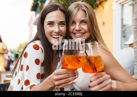 Bild von fröhlichen Erwachsenen zwei Frauen lachen und umarmen während Trinken Cocktails am Tisch im Café im Freien Stockfoto