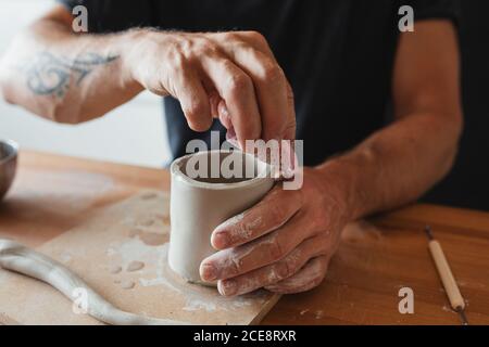 Nicht erkennbarer Keramiker mit Ton und die Schaffung Tasse während des Sitzens Tisch und Arbeiten in der Werkstatt Stockfoto