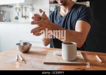 Nicht erkennbarer Keramiker mit Ton und die Schaffung Tasse während des Sitzens Tisch und Arbeiten in der Werkstatt Stockfoto