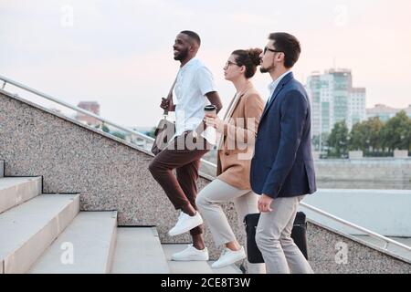Seitenansicht selbstbewusster multiethnischer Studenten, die sich unterhalten und aufziehen Treppen, wenn man zur Universität läuft Stockfoto