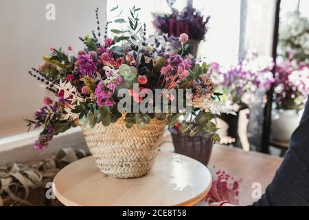 Bündel von verschiedenen frischen bunten Blumen in rosa und lila Töne in Korbkorb auf Holztisch in gesetzt komponiert Modernes Floristik-Geschäft Stockfoto