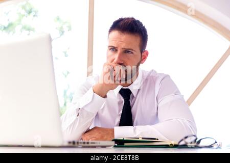 Aufnahme eines enttäuschten Geschäftsmannes, der während der Arbeit hinter seinem Laptop am Schreibtisch saß. Heimbüro. Stockfoto