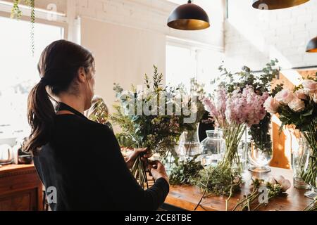 Rückansicht der konzentrierten weiblichen Designerin Anordnung dekorative blühende Blumensträuße Während der Arbeit auf Bestellung für Veranstaltung in kreativen Floristik Studio Stockfoto