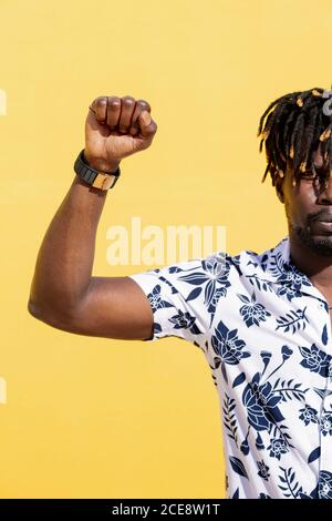 Vertikales Foto eines attraktiven jungen schwarzen Mannes mit erhobener Faust auf intensivem gelben Hintergrund, Konzept von Menschenrechtskampf und Lebensstil, Kopierraum für Text Stockfoto
