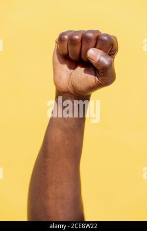 Vertikales Foto einer erhobenen Faust eines schwarzen Mannes auf einem intensiv gelben Hintergrund, Konzept von Menschenrechtskampf und Lebensstil Stockfoto