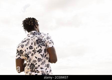 Rückansicht eines stylischen jungen afroamerikaners in einem Blumenshirt mit dem Himmel im Hintergrund, Konzept von Freiheit und Lifestyle, Kopierraum für Text Stockfoto