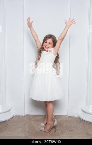 Kleine Prinzessin - aufgeregt emotionale niedliche Mädchen in Mode weiß Kleid mit Spaß und tragen große Mütter funkeln High Heels Schuhe auf weißem Hintergrund Stockfoto