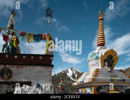 Buddhistische Stupa mit Gebetsfahnen, die den schneebedeckten Himalaya unter blauem Himmel zwischen Manali und Kaza, Himachal Pradesh, Indien, überragen. Stockfoto