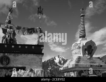 Buddhistische Stupa mit Gebetsfahnen, die den schneebedeckten Himalaya unter blauem Himmel zwischen Manali und Kaza, Himachal Pradesh, Indien, überragen. Stockfoto