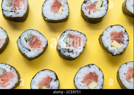 Blick von oben auf leckere Sushi-Brötchen mit Reis und Lachs Platziert auf bunten gelben Tisch mit Essstäbchen im Studio Stockfoto
