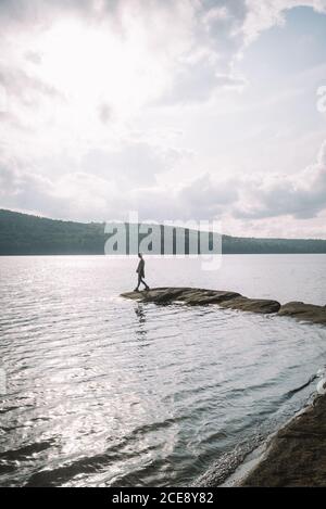 Rückansicht eines anonymen Wanderers, der an steinernen Ufern steht In der Nähe von ruhigen See und genießen Sie die Freiheit während der bewölkten Sommertag Im Algonquin Provincial Park in Kanada Stockfoto