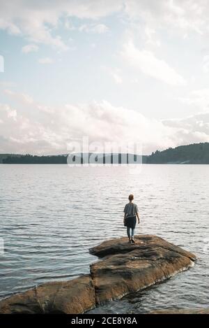 Rückansicht einer anonymen Wanderin, die an steinernen Ufern steht In der Nähe von ruhigen See und genießen Sie die Freiheit während der bewölkten Sommertag Im Algonquin Provincial Park in Kanada Stockfoto