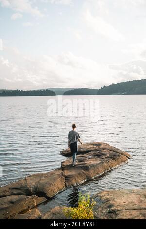 Rückansicht eines anonymen Wanderers, der an steinernen Ufern steht In der Nähe von ruhigen See und genießen Sie die Freiheit während der bewölkten Sommertag Im Algonquin Provincial Park in Kanada Stockfoto