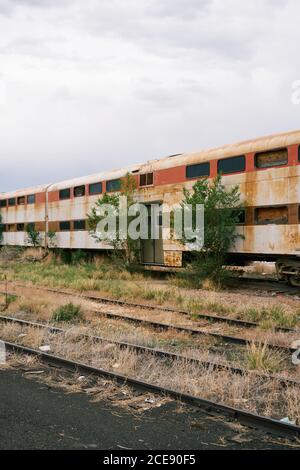 Alter Zug mit rostiger Metallfassade auf vergessener Eisenbahn An bewölktem Tag in den USA Stockfoto