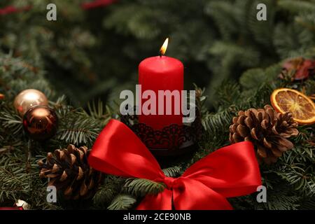 Nahaufnahme einer Reihe von Weihnachtsdekorationen mit einer brennenden Kerze, Tannenzweigen und Zapfen Stockfoto