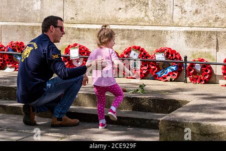 Ein kleines Mädchen stellt eine Blume am Fuße des Kriegsdenkmals im Zentrum von Harrogate, nachdem es zwei Minuten Stille zu Ehren der Gefallenen beobachtet hat. Stockfoto