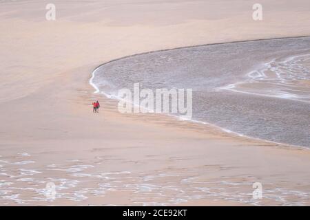 Spaziergänger, die bei Ebbe über den Strand von Crantock spazieren, während der Fluss Gannel in Newquay in Cornwall zum Meer fließt. Stockfoto