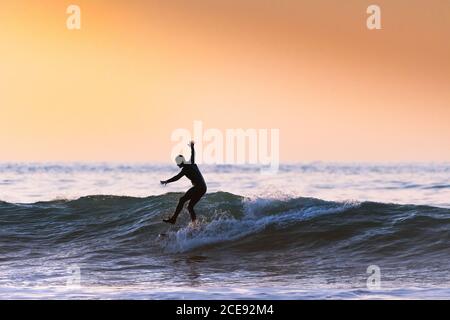 Ein Surfer, der auf einer Welle reitet und abends im Fistral in Newquay in Cornwall auf einem Bein steht. Stockfoto