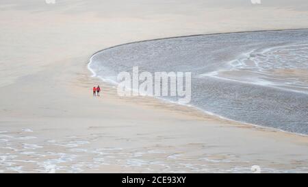 Ein Panoramabild von Spaziergängern, die bei Ebbe über den Crantock Beach in Newquay in Cornwall laufen. Stockfoto