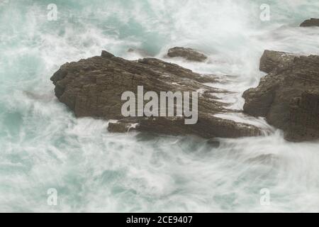 Von oben Schuss der Wellen des majestätischen Meeres Rollen um†rauh Schwarze Steinoberfläche in Kantabrien Stockfoto