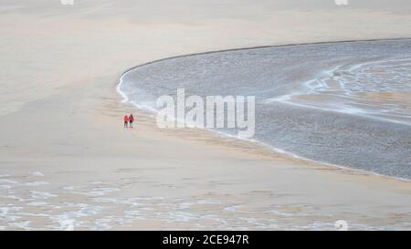 Ein Panoramabild von Spaziergängern, die bei Ebbe über Crantock Beach laufen, während der Fluss Gannel in Newquay in Cornwall zum Meer fließt. Stockfoto