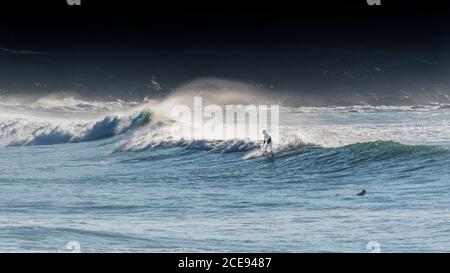 Ein Panoramabild eines Surfers, der eine Welle am South Fistral in Newquay in Cornwall reitet. Stockfoto