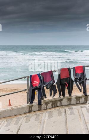 RNLI Rettungsschwimmer-Neoprenanzüge drapierten über einen Handlauf, um am Fistral Beach in Newquay in Cornwall zu trocknen. Stockfoto