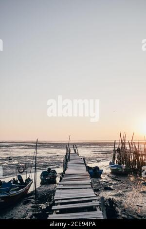 Perspektivischer Blick auf alten hölzernen Pier auf schlammigem Ufer mit festverankerten Booten im Sonnenlicht, Portugal Stockfoto