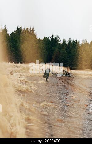 Seitenansicht einer anonymen Person, die auf einem grauen Kiesstrand an der Küste mit immergrünen Wäldern im Hintergrund steht. Stockfoto