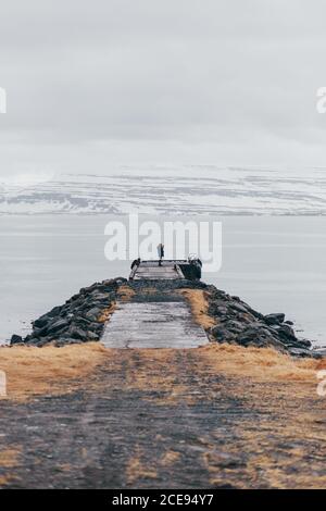 Rückansicht eines Mannes mit Kamera, der auf dem Pier gegen die verschneite Strecke im Nebel steht, Island. Stockfoto