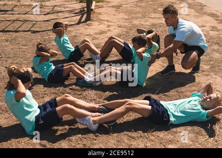 Männliche Fitness-Trainer instructing, während Kinder Durchführung Sit-ups an Ein Boot Camp Stockfoto